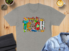 Load image into Gallery viewer, Grey t-shirt with "made to TEACH" text design featuring school supplies.
