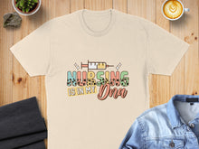 Load image into Gallery viewer, Cream t-shirt with colorful "Nursing is in my DNA" text and syringe graphic.
