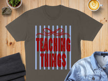 Load image into Gallery viewer, Brown t-shirt with red "Teaching Things" text and a bow on a striped background.

