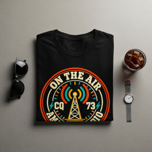 Load image into Gallery viewer, Black t-shirt with "On The Air" design featuring a radio tower, CQ, 73, and American Radio.
