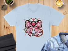 Load image into Gallery viewer, Light blue t-shirt with a pink bow featuring XOXO hearts, stethoscope, and nurse hat.
