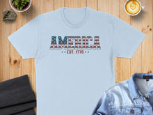 Load image into Gallery viewer, Light blue t-shirt with "AMERICA EST. 1776" printed in a distressed American flag design.
