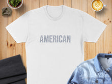 Load image into Gallery viewer, White t-shirt with "AMERICAN" text design on the front, laid flat on a wooden surface.
