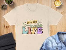 Load image into Gallery viewer, Cream t-shirt with colorful "livin' the scrub life" text and stethoscope graphic.
