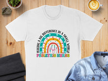 Load image into Gallery viewer, Rainbow graphic with stethoscope and text "MAKING A BIG DIFFERENCE IN A SMALL WORLD PEDIATRIC NURSE" on a white t-shirt.
