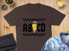 Load image into Gallery viewer, Brown t-shirt with "ABCD" text in yellow lightning bolt and black checkerboard design.
