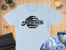 Load image into Gallery viewer, Light blue t-shirt with black "America EST. 1776" circular graphic.
