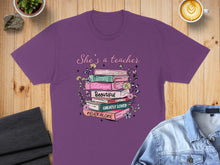 Load image into Gallery viewer, Purple t-shirt with "She's a teacher" and inspirational words in a book stack.
