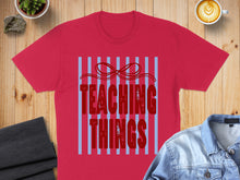 Load image into Gallery viewer, Red t-shirt with "TEACHING THINGS" text on blue striped background.
