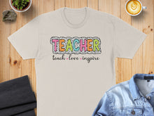 Load image into Gallery viewer, Beige t-shirt with "TEACHER" in colorful block letters and "teach love inspire" below.
