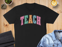 Load image into Gallery viewer, Black t-shirt with colorful "TEACH" text, framed by coffee and denim.

