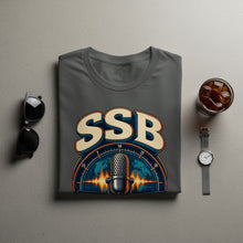 Load image into Gallery viewer, Dark grey t-shirt with SSB logo featuring microphone and world map design.
