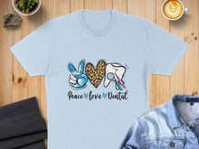 Load image into Gallery viewer, Light blue t-shirt with "Peace Love Dental" text and dental icons.
