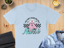 Load image into Gallery viewer, Ghost nurse costume graphic with text "You can't scare me I'm a Nurse" on a light blue t-shirt.
