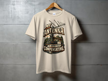 Load image into Gallery viewer, Cream t-shirt with "My Antenna Is Definitely Compensating" text and illustration.

