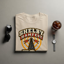 Load image into Gallery viewer, Beige t-shirt with "Shelby Hamfest" text and radio tower graphic.
