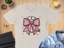 Load image into Gallery viewer, Pink bow with stethoscope and hearts, on a tan t-shirt.
