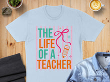 Load image into Gallery viewer, Light blue t-shirt with "THE LIFE OF A TEACHER" text and a pencil graphic.
