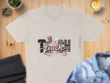 Load image into Gallery viewer, Light tan t-shirt with "TEACH" design featuring leopard print, plaid, and school icons.
