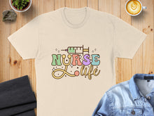 Load image into Gallery viewer, Nurse Life text with syringe and colorful stars, on a cream t-shirt.

