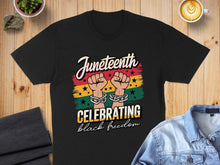 Load image into Gallery viewer, Black t-shirt with "Juneteenth Celebrating black freedom" text and linked fists graphic.
