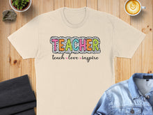 Load image into Gallery viewer, Cream t-shirt with "Teacher teach love inspire" text in colorful, playful font.
