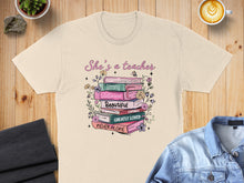 Load image into Gallery viewer, T-shirt with stack of books, floral accents, and text "She's a teacher".
