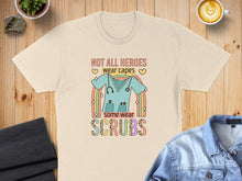 Load image into Gallery viewer, Cream t-shirt with "Not all heroes wear capes, some wear scrubs" and scrub top graphic.
