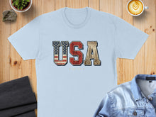 Load image into Gallery viewer, Light blue t-shirt with "USA" text featuring American flag and city skyline design.
