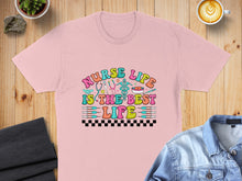 Load image into Gallery viewer, Pink t-shirt with colorful "Nurse Life Is The Best Life" text and medical icons.
