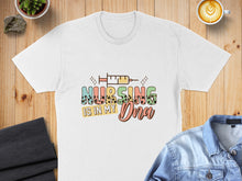 Load image into Gallery viewer, White t-shirt with "Nursing is in my DNA" graphic featuring a syringe and sparkly accents.
