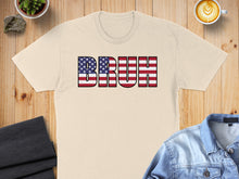 Load image into Gallery viewer, Beige t-shirt with "BRUH" in American flag letters on a wooden surface.
