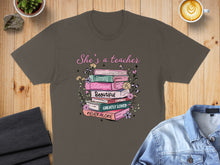 Load image into Gallery viewer, T-shirt with stack of books: "She's a teacher," "Strong," "Victorious," "Beautiful," "Capable," "Greatly Loved," "Never Alone."
