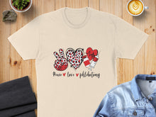 Load image into Gallery viewer, Cream t-shirt with "Peace love phlebotomy" design featuring heart and syringe graphics.
