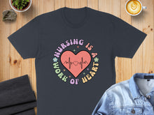 Load image into Gallery viewer, T-shirt with "Nursing is a work of heart" text and heart monitor graphic.
