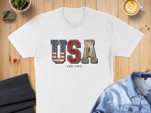 Load image into Gallery viewer, White t-shirt with USA text graphic featuring US flag and city skyline.
