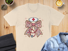 Load image into Gallery viewer, Cream t-shirt with nurse-themed graphic of a stethoscope and bow with crosses and "XOXO".
