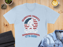 Load image into Gallery viewer, Light blue t-shirt with Bigfoot, American flag, and "Celebrating America's Semiquincentennial 1776-2026".

