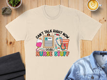 Load image into Gallery viewer, Cream t-shirt with "Can't Talk Right Now Doing Nurse Stuff" graphic.
